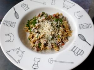 Creamy mascarpone pasta with ham, mushrooms, red pepper and herbs served in a bowl.