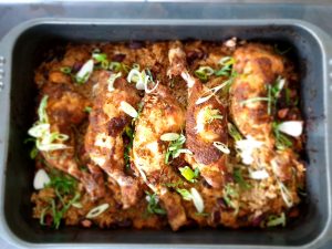 Jerk chicken legs baked on top of rice and peas in a roasting tray, with golden skin, visible spices, and fluffy rice cooked in coconut milk and stock.