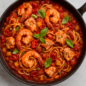 Salmon and prawn pasta in a rich tomato sauce with peppers, chillies and capers, served in a pan with visible chunks of flaked salmon and whole prawns